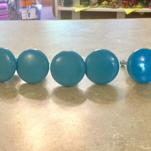 K&ouml;nnte beinhalten: F&uuml;nf tealblaue Holzkn&ouml;pfe mit silbernen Schrauben. Die Kn&ouml;pfe sind rund und haben eine glatte Oberfl&auml;che.