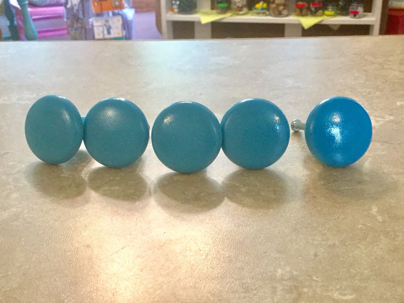 K&ouml;nnte beinhalten: F&uuml;nf tealblaue Holzkn&ouml;pfe mit silbernen Schrauben. Die Kn&ouml;pfe sind rund und haben eine glatte Oberfl&auml;che.