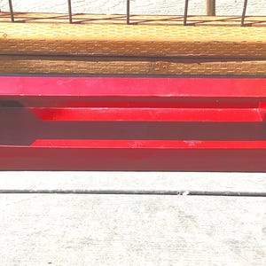 May include: A bright red metal toolbox with a rectangular shape and a handle opening. The toolbox is empty and sits on a wooden surface, with a wooden fence in the background. The toolbox is designed for storing tools.