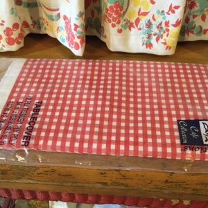 May include: A packaged red and white gingham tablecloth. The package includes the text "TABLECOVER" and measurements of 1.37 m x 2.74 m. The tablecloth is from the Cafe Collection Sensations.