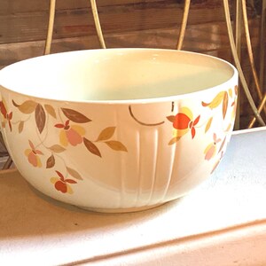 May include: A round, off-white ceramic bowl featuring a repeating floral pattern in shades of orange, yellow, and brown. The exterior of the bowl is decorated with vertical ribbed indentations that break up the floral design around the circumference.