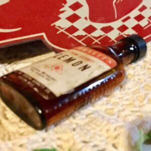 May include: A brown glass bottle with a white label that says "LEMON" and "Bennett's" on it. The bottle is sitting on a white crocheted surface.