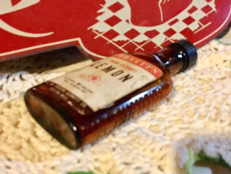 May include: A brown glass bottle with a white label that says "LEMON" and "Bennett's" on it. The bottle is sitting on a white crocheted surface.
