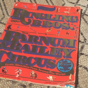 May include: A red, white, and blue program for the Ringling Bros. and Barnum & Bailey Circus. The program features a globe with the text "Exotic Attractions From Around The World!" and a variety of circus performers in the background.