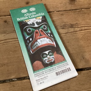 May include: A green travel guide for Alberta and British Columbia, featuring a colorful totem pole on the cover. The guide is published by the American Automobile Association and the Canadian Automobile Association. The text on the cover reads "Retail Value $2.75".
