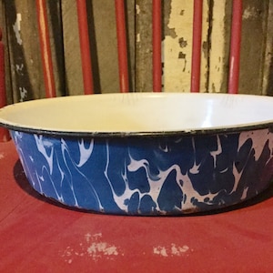 May include: A blue and white enamelware bowl with a marbled pattern. The bowl has a black rim and is slightly chipped on the edge.