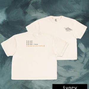 Puede incluir: Camisetas de color marfil con texto negro y un gr&aacute;fico de monta&ntilde;a. Una camiseta muestra el texto "$ gh push" y "push me into traffic". La otra camiseta tiene un gr&aacute;fico de monta&ntilde;a y el texto "-good vibe".