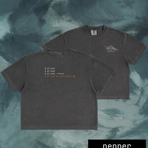 Puede incluir: Dos camisetas de color gris oscuro. Una camiseta muestra el texto "$ gh push", "$ gh push", "$ gh push --force" y "$ gh push me into traffic |". La otra camiseta tiene un gr&aacute;fico de monta&ntilde;a y el texto "MOUNTAIN TRIBE". La palabra "pepper" est&aacute; en la parte inferior.
