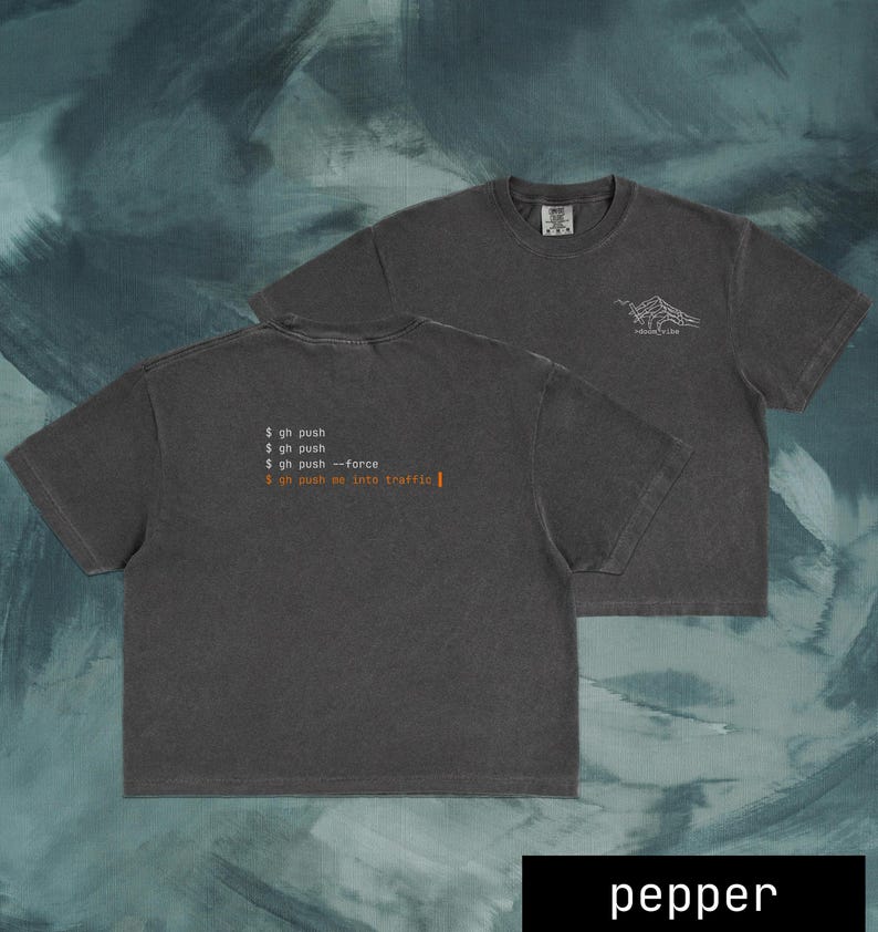 Puede incluir: Dos camisetas de color gris oscuro. Una camiseta muestra el texto "$ gh push", "$ gh push", "$ gh push --force" y "$ gh push me into traffic |". La otra camiseta tiene un gr&aacute;fico de monta&ntilde;a y el texto "MOUNTAIN TRIBE". La palabra "pepper" est&aacute; en la parte inferior.