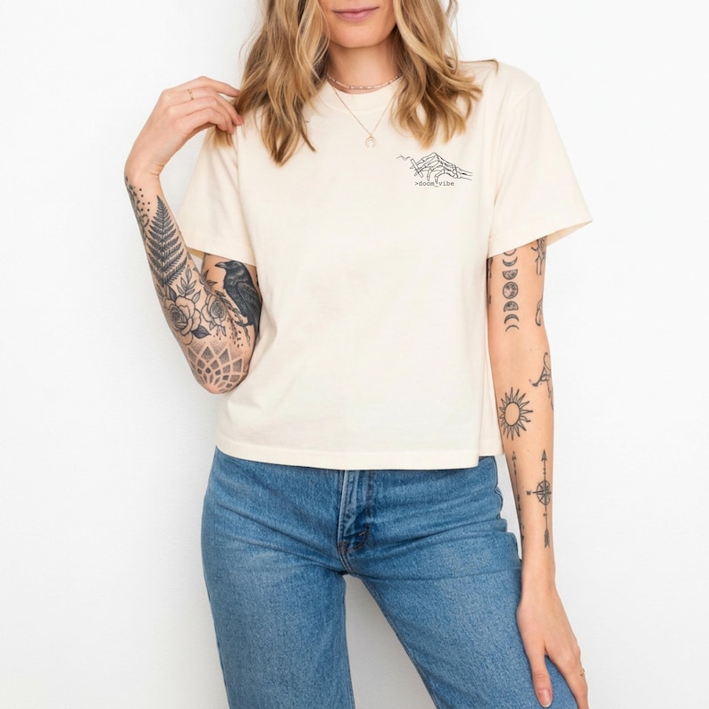 Puede incluir: Camiseta color crema con un gr&aacute;fico de monta&ntilde;a negro y el texto "desert vibe". La camiseta de manga corta se combina con unos vaqueros azules. La imagen muestra a una persona que lleva la camiseta.
