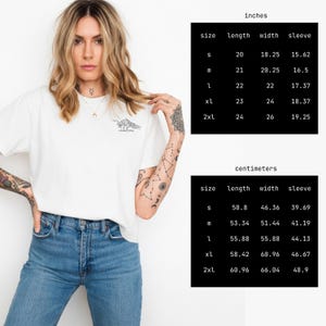 Puede incluir: Camiseta blanca con un gr&aacute;fico de monta&ntilde;a y el texto "Mountain Vibe". La imagen incluye una tabla de tallas en cent&iacute;metros, con medidas de largo, ancho y manga para las tallas S a 2XL.