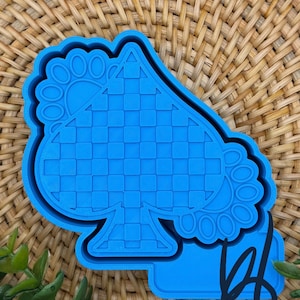 May include: A vibrant blue cookie cutter shaped like a spade playing card suit. The spade design features a checkered pattern and a decorative border. The cutter is made of plastic and is set against a woven background.