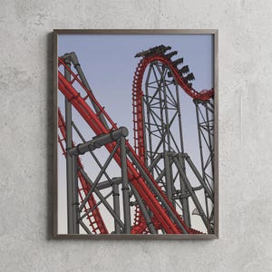 May include: A framed art print featuring a stylized illustration of a roller coaster with bright red tracks and dark gray steel support beams against a pale blue sky. The coaster structure includes steep vertical climbs and sharp curves.