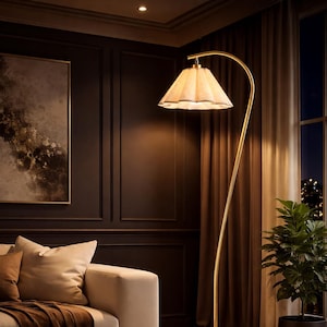 Peut inclure: Un lampadaire dor&eacute; avec une tige incurv&eacute;e et un abat-jour &agrave; volants &eacute;claire un salon. La pi&egrave;ce comprend un canap&eacute; aux tons neutres, une table basse ronde et une plante en pot. Les murs sont brun fonc&eacute; avec des panneaux d&eacute;coratifs.