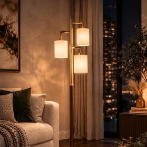 May include: A three-light floor lamp with a gold finish and cream shades. The lamp has a dark brown wooden pole and a round base. The lamp is in a living room setting with a sofa, rug, and side table. The lamp's height is approximately 170 cm.