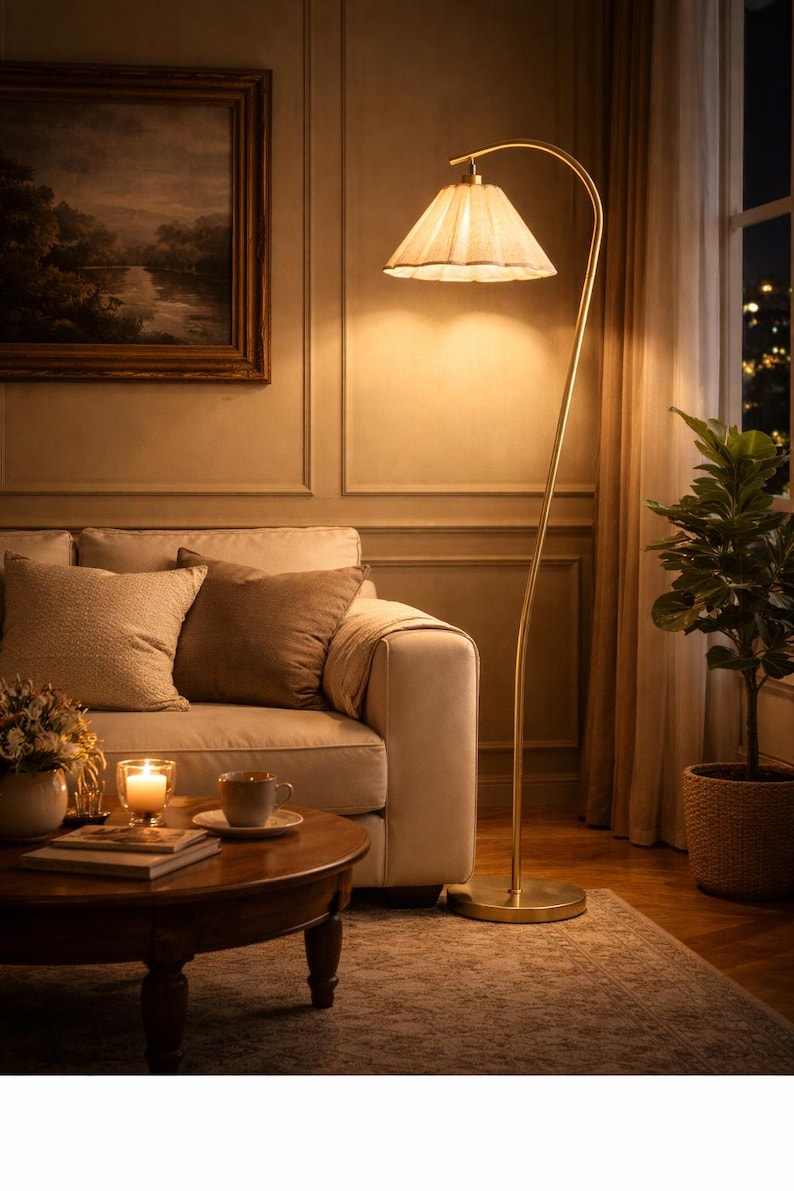 Peut inclure: Un lampadaire dor&eacute; en arc avec un abat-jour pliss&eacute; &eacute;claire un salon. La pi&egrave;ce comprend un canap&eacute; avec des coussins, une table basse ronde et une peinture de paysage encadr&eacute;e. Une plante en pot est pr&egrave;s d'une fen&ecirc;tre.