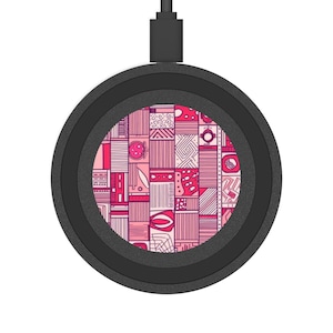 May include: A black wireless charger with a pink and white geometric pattern in the center. The charger has a circular design with a USB-C cable attached. The pattern features various shapes and lines.