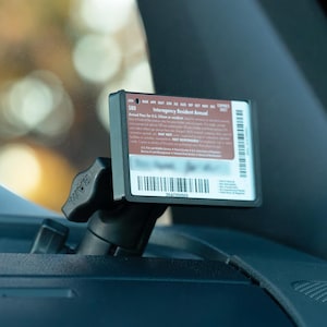 May include: A black holder with a card is mounted on a vehicle dashboard. The card has text that reads "Interagency Resident Annual" and a barcode. The holder is attached to a black adjustable arm.