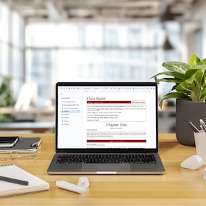 May include: A silver laptop displaying a document with the text Class Name and Chapter Title on its screen. The laptop sits on a wooden desk alongside a spiral notebook, a black pen, a white correction fluid, a potted green plant, and a pen holder.