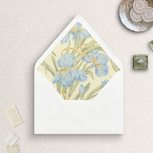 May include: A white envelope with an open flap revealing an interior liner featuring a botanical pattern of light blue iris flowers with yellow centers and green stems on a pale cream background, accompanied by wax seals and a ring in a box.