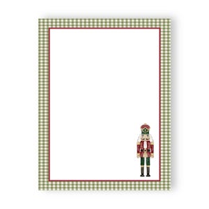 May include: A rectangular stationery sheet featuring a white center bordered by a thin red line and a wider outer frame with a green and white gingham pattern. A small, detailed illustration of a nutcracker stands in the bottom right corner.