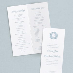 May include: Elegant wedding stationery set featuring a program and invitation. The program lists the order of service and wedding party details. The invitation includes the names of the couple and wedding details, all in a soft blue script.