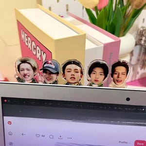 May include: A laptop with five face stickers of young people. Two decorative book-shaped boxes are behind the laptop. The boxes are light yellow and pink with the word "HERGRY" on one and "Rhych" on the other.