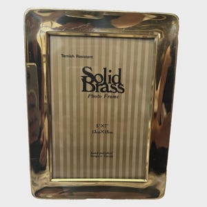 May include: A rectangular solid brass photo frame with a polished gold-tone finish. The insert features the text Tarnish Resistant, Solid Brass Photo Frame, 5x7 inches, 13cmx18cm, and hand-polished lacquer finish over a beige vertical striped background.
