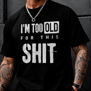 May include: A black short-sleeved t-shirt featuring white distressed-style text that reads I'M TOO OLD FOR THIS SHIT. The design is centered on the chest, with the word OLD highlighted in a white rectangular box and SHIT in a larger font.