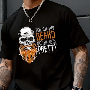 Könnte beinhalten: Ein schwarzes Kurzarm-T-Shirt mit einer Grafik eines Totenkopfes mit langem orangefarbenem Bart. Der Text lautet "TOUCH MY BEARD AND TELL ME I'M PRETTY", wobei "BEARD" in Orange und die restlichen Wörter in Weiß in einer zerklüfteten Schriftart.