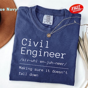 May include: A navy blue t-shirt with the words "Civil Engineer" in white, a pronunciation guide, and the phrase "Making sure it doesn't fall down." A gold necklace and a "Fast Delivery" sticker are also visible.