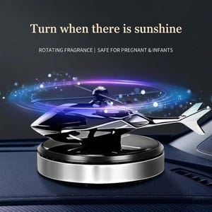 Puede incluir: Un ambientador para coche con forma de helicóptero negro y plateado. El ambientador tiene una función de fragancia giratoria y es seguro para mujeres embarazadas y bebés. El texto de la imagen dice: "Gira cuando haya sol."