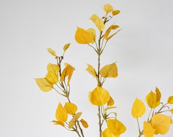 May include: A single artificial stem with multiple branches and yellow leaves. The leaves are a vibrant yellow color, and the stem is a dark brown. The leaves are oval-shaped and arranged along the branches. The stem is against a white background.