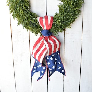 May include: A green boxwood wreath with a red, white, and blue American flag ribbon.