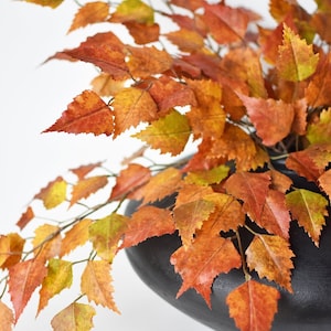 May include: A black vase filled with a bouquet of fall foliage. The leaves are a mix of orange, yellow, and green.