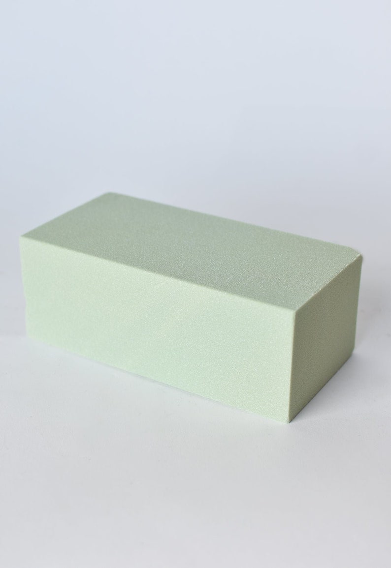 May include: A rectangular, light green floral foam brick. The foam has a textured surface and is designed for arranging flowers. The block is a solid, rectangular shape, perfect for creating floral displays.