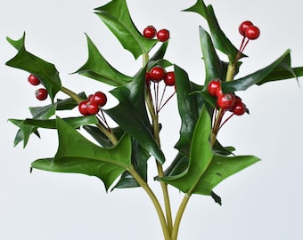 May include: A sprig of artificial holly with glossy green leaves and clusters of bright red berries. The leaves have a distinctive, spiky shape. The stems are bundled together and tied with twine, creating a festive, seasonal decoration.