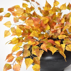 May include: A black ceramic vase filled with a bouquet of yellow and orange autumn leaves.