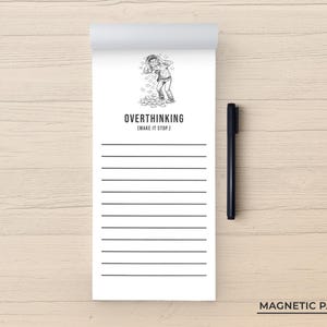 May include: A white magnetic notepad with the words "OVERTHINKING (MAKE IT STOP.)" and a black pen. The notepad has a black and white illustration of a person with their hands on their head. The notepad has horizontal lines.