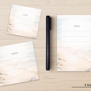 May include: Three rectangular paper note pads featuring a beach scene with sand, seashells, and ocean waves. Each pad has the word NOTES printed at the top with horizontal lines for writing. A black felt-tip pen is positioned vertically between them.