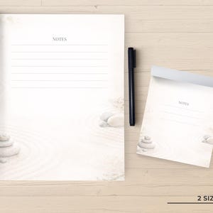 May include: A large notepad and a smaller notepad, both featuring a light-colored zen garden design with stacked stones and raked sand patterns. Each notepad has the word NOTES printed at the top above horizontal lines. A black pen is included.