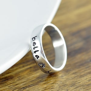 Peut inclure: Bague en argent gravée du mot "bella" et d'une empreinte de patte.