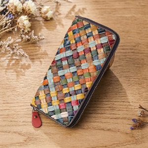 May include: A colorful, woven leather wallet with a zipper closure. The wallet features a patchwork design with various colors, including blue, green, orange, and yellow. The zipper pull is red. The wallet is rectangular and appears to be made of high-quality leather.