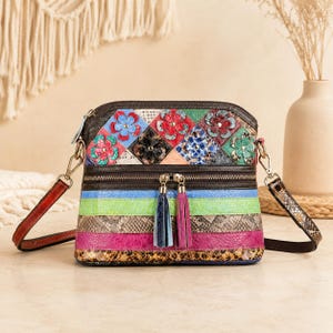 May include: A multi-colored crossbody bag featuring a top panel with floral appliques and a lower section with horizontal stripes in blue, green, brown, pink, and snakeskin textures. The bag includes two tassels and a detachable shoulder strap.
