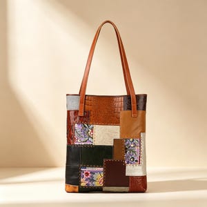 May include: A vertical tote bag featuring a patchwork design of various leather textures and floral fabric panels. The bag includes two long brown leather shoulder straps and is constructed from rectangular pieces in shades of brown, black, and cream.