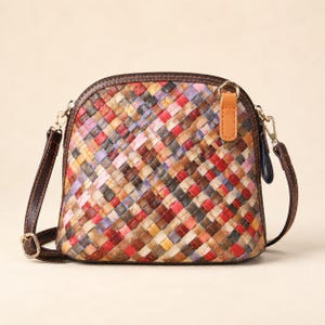 May include: A dome-shaped crossbody bag featuring a multi-colored woven pattern in shades of red, yellow, blue, purple, and brown. The bag has dark brown leather-like trim, a light tan zipper pull tab, and an adjustable dark brown shoulder strap.