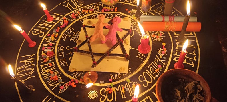 Puede incluir: Un mantel de altar circular negro con un dise&ntilde;o blanco de la rueda del a&ntilde;o que incluye texto como Samhain, Yule y Summer Solstice. Dos peque&ntilde;as figuras de arcilla se encuentran dentro de un pentagrama de ramas sobre una tarjeta cuadrada blanca.