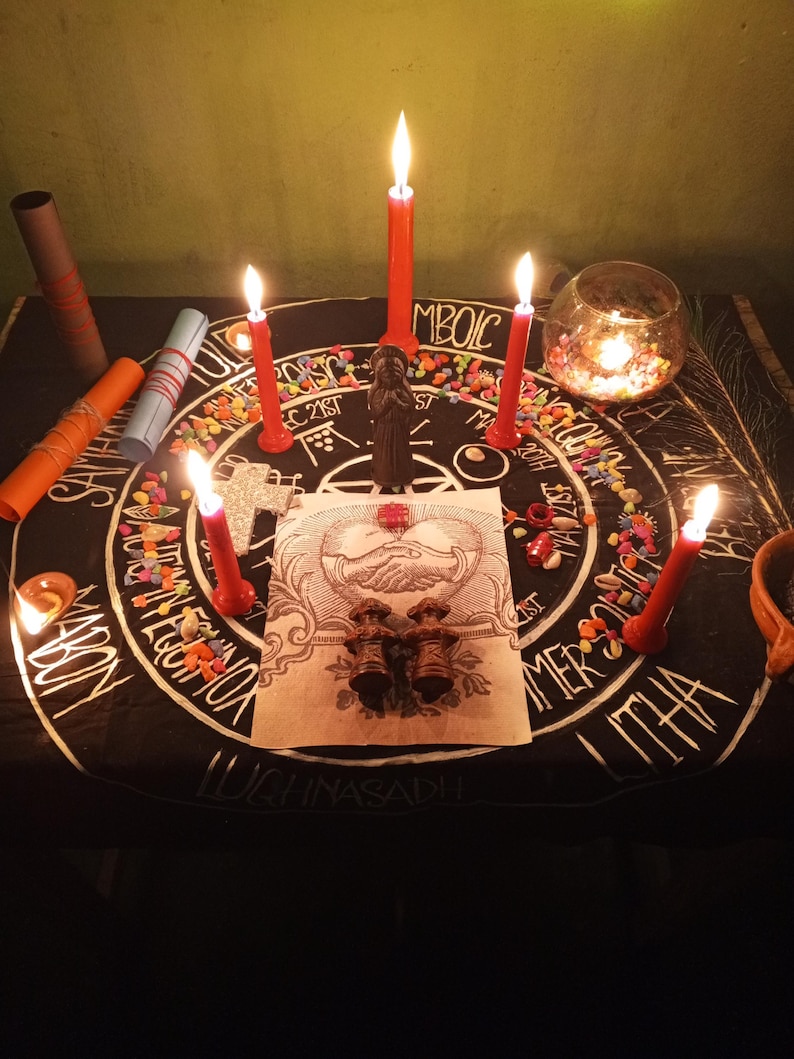 Puede incluir: Un altar ritual con una tela negra con un dise&ntilde;o circular blanco y texto. Se encienden velas rojas alrededor del altar, con una peque&ntilde;a estatua y otros objetos. Tambi&eacute;n hay piedras de colores y un candelabro de cristal.