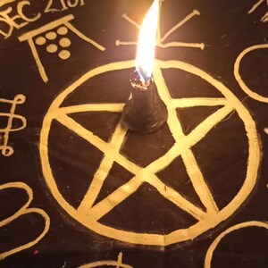 K&ouml;nnte beinhalten: Eine schwarze Oberfl&auml;che mit goldenen Symbolen, darunter ein Pentagramm, ein Kreuz und andere esoterische Designs. Eine brennende schwarze Kerze befindet sich in der Mitte. Die Worte "DEC 21st" und "MARCH 20th" sind sichtbar.