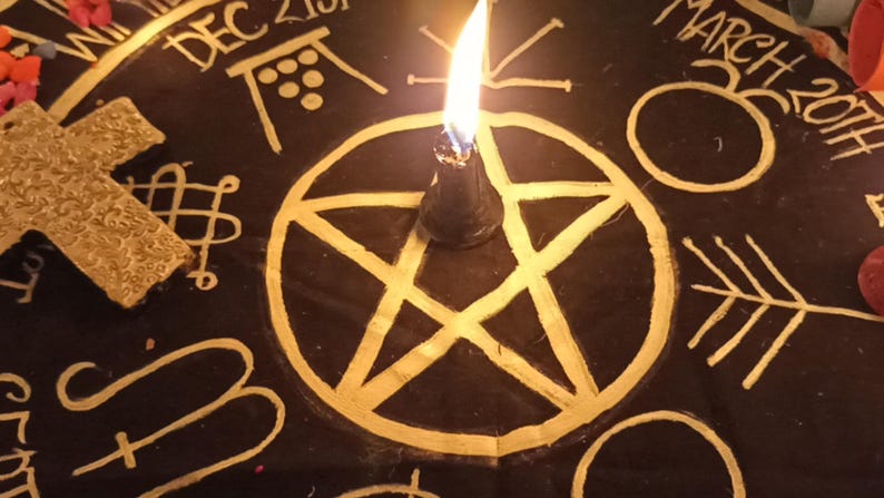 K&ouml;nnte beinhalten: Eine schwarze Oberfl&auml;che mit goldenen Symbolen, darunter ein Pentagramm, ein Kreuz und andere esoterische Designs. Eine brennende schwarze Kerze befindet sich in der Mitte. Die Worte "DEC 21st" und "MARCH 20th" sind sichtbar.